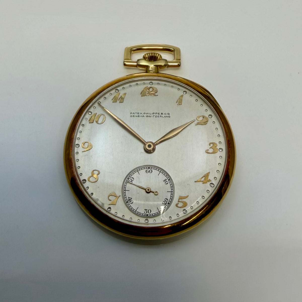 Patek Philippe pocket watch with a pale dial, gold-tone numerals, and a small seconds subdial.