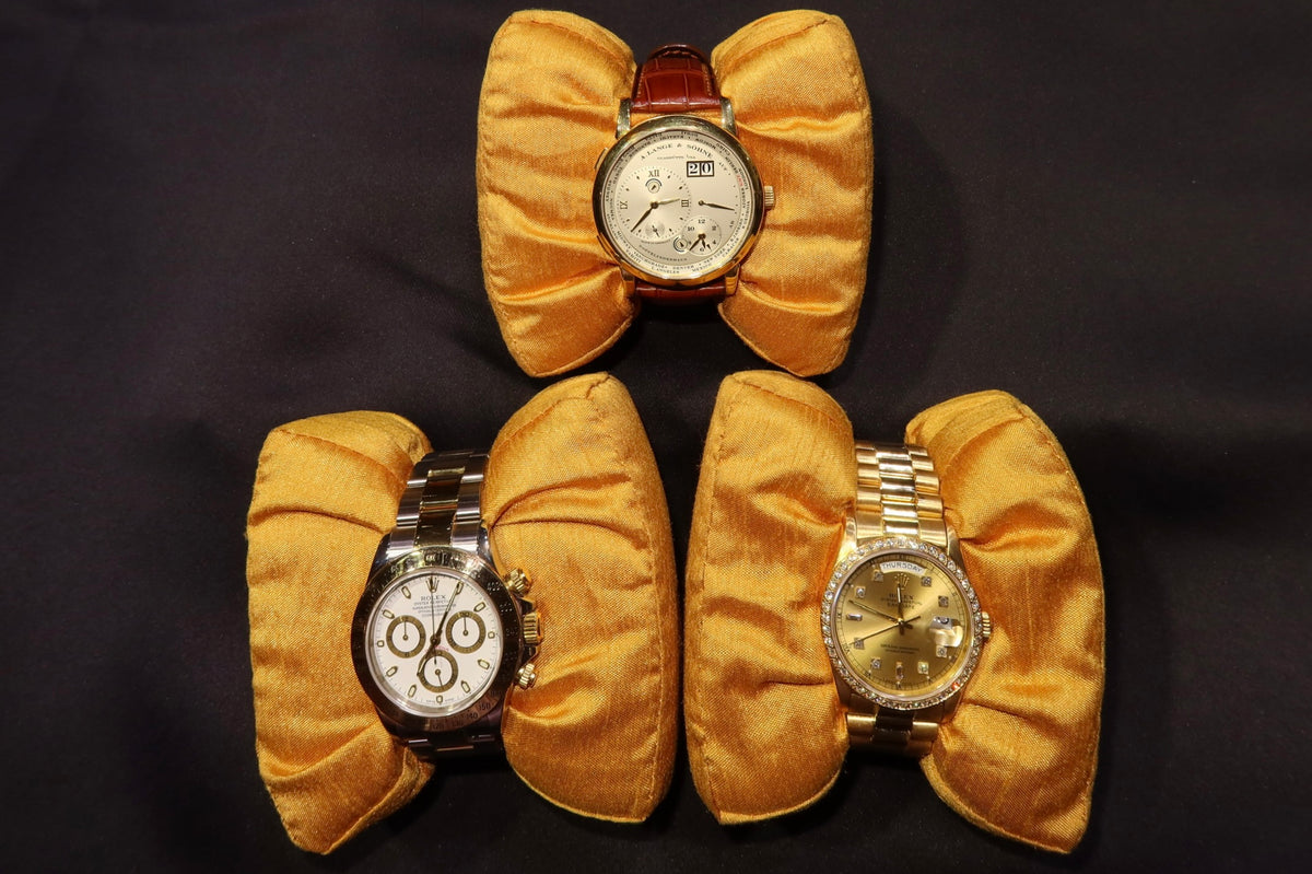 Explore vintage wristwatches: three watches with a leather strap and metal bracelets on gold cushions.